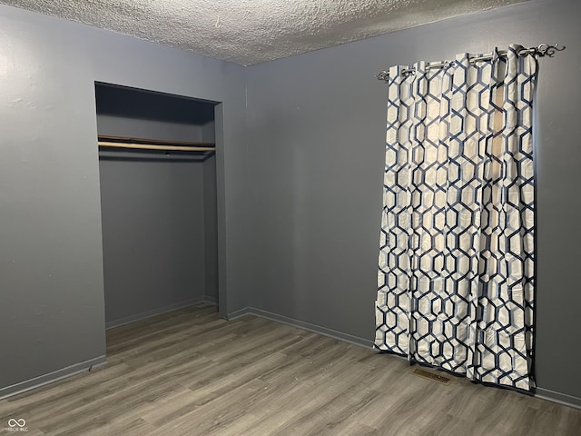 unfurnished bedroom featuring a closet, a textured ceiling, visible vents, and wood finished floors