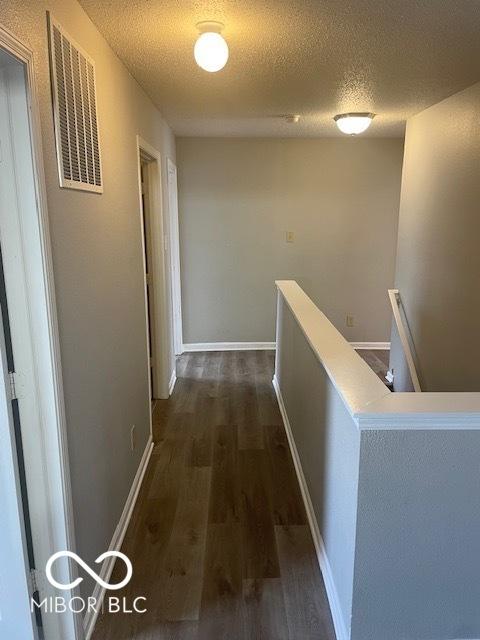 8249 Retreat Ln, Indianapolis, IN 46259 - hall featuring an upstairs landing, a textured ceiling, dark wood-style floors, baseboards, and visible vents