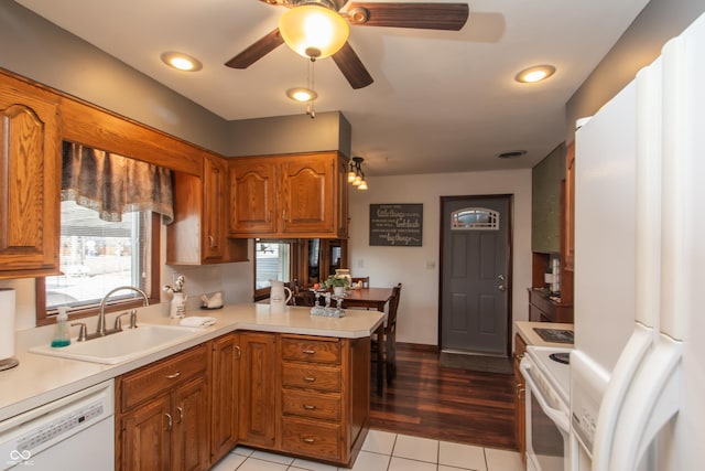 kitchen featuring brown cabinets, light countertops, a sink, white appliances, and a peninsula