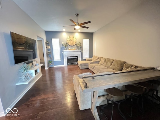 living area with a ceiling fan, dark wood finished floors, a fireplace, and baseboards