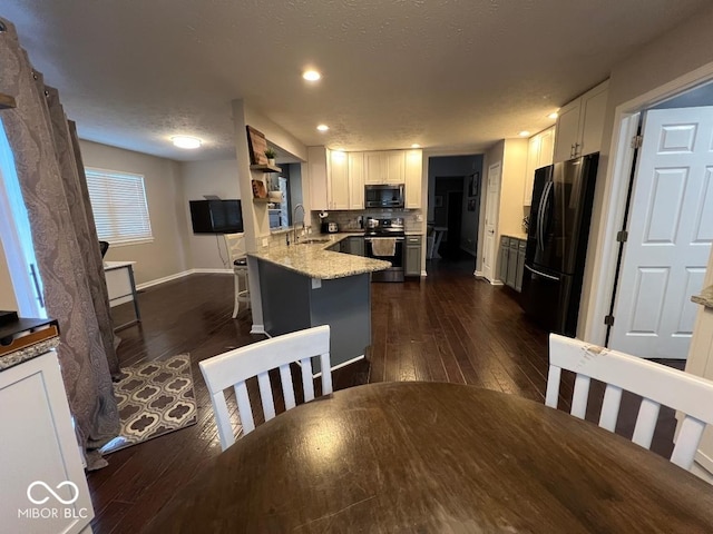 kitchen featuring appliances with stainless steel finishes, dark wood-type flooring, white cabinetry, a peninsula, and a kitchen breakfast bar