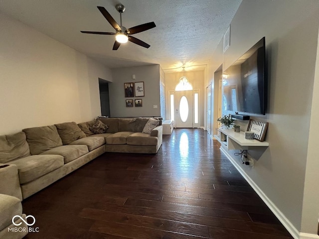 living area featuring a textured ceiling, ceiling fan, dark wood-type flooring, and baseboards