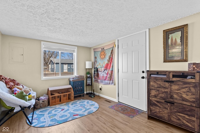 foyer entrance featuring a textured ceiling, wood finished floors, electric panel, and baseboards