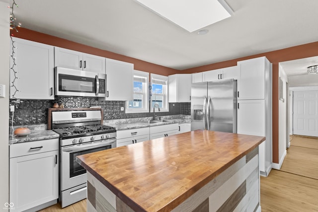 kitchen with appliances with stainless steel finishes, a sink, butcher block counters, and white cabinets