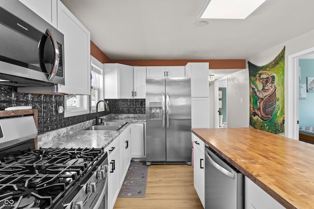 kitchen with stainless steel appliances, white cabinetry, a sink, and wooden counters