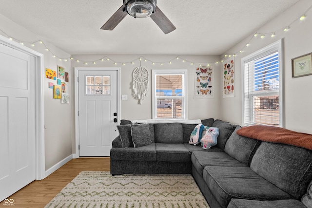 living area with light wood-type flooring, ceiling fan, a textured ceiling, and baseboards