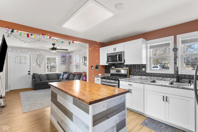 kitchen with butcher block counters, appliances with stainless steel finishes, white cabinetry, a sink, and light wood-type flooring