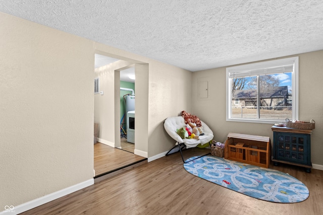 living area featuring a textured ceiling, baseboards, wood finished floors, and a textured wall