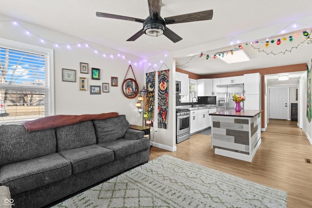 living area with light wood finished floors, ceiling fan, and baseboards