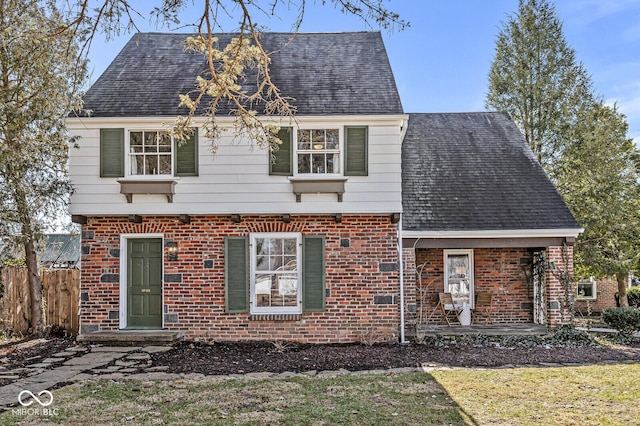 view of front of property with a shingled roof, brick siding, and fence