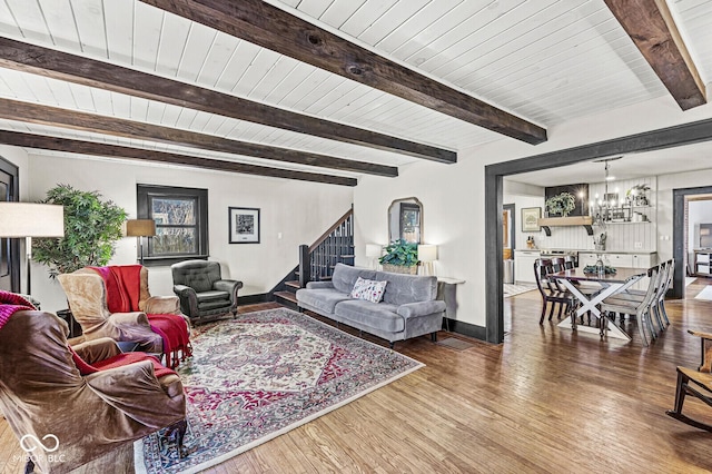 living area with an inviting chandelier, stairs, wood finished floors, and beamed ceiling