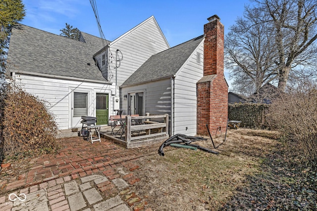 back of house featuring a patio, a shingled roof, and a chimney