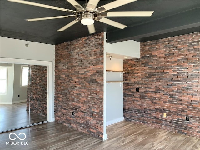 spare room featuring beam ceiling, brick wall, and wood finished floors