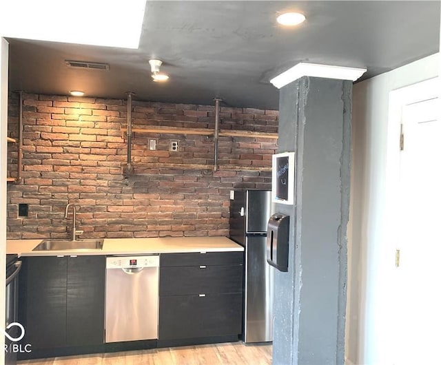 kitchen featuring appliances with stainless steel finishes, visible vents, a sink, and brick wall