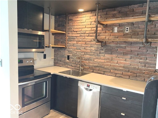 kitchen with stainless steel appliances, light countertops, a sink, brick wall, and modern cabinets