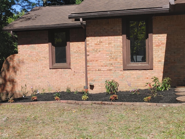 view of property exterior featuring brick siding, a lawn, and a shingled roof