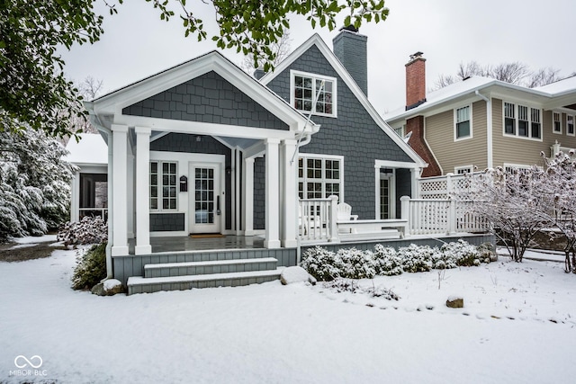 snow covered back of property with covered porch and a chimney