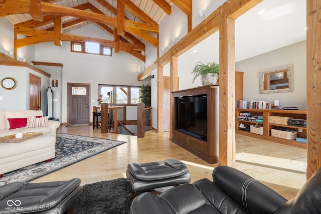 living area featuring high vaulted ceiling, a glass covered fireplace, beamed ceiling, and wood finished floors