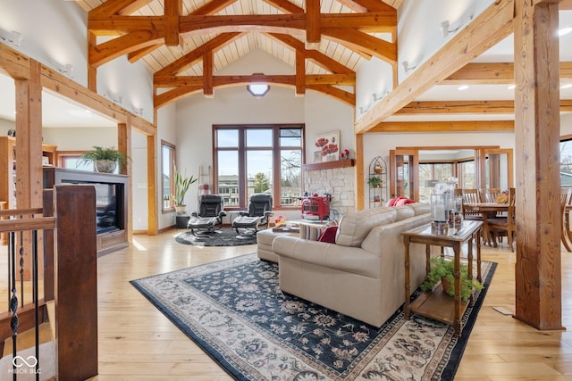 living room featuring light wood finished floors, high vaulted ceiling, and a stone fireplace