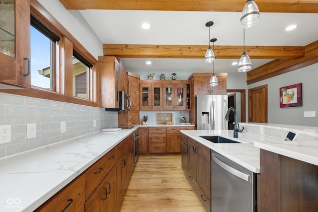 kitchen with appliances with stainless steel finishes, brown cabinetry, a sink, and beamed ceiling