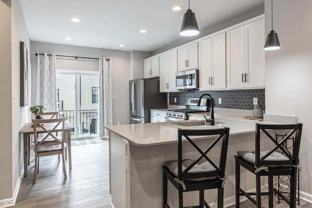 kitchen with tasteful backsplash, white cabinets, appliances with stainless steel finishes, light countertops, and light wood-style floors