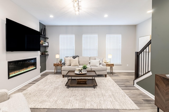 living room featuring recessed lighting, stairway, a glass covered fireplace, wood finished floors, and baseboards