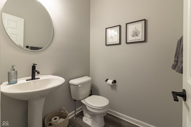 half bath with toilet, baseboards, and wood finished floors