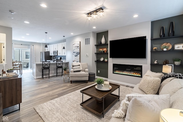 living room featuring recessed lighting, visible vents, baseboards, light wood-style floors, and a glass covered fireplace