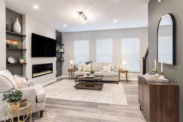 living area with a glass covered fireplace, baseboards, light wood finished floors, and recessed lighting