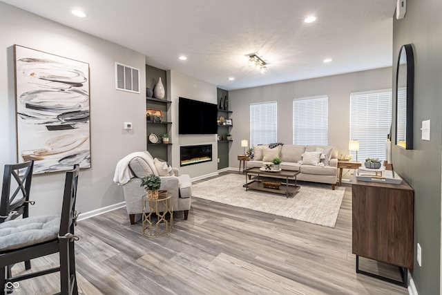 living area with light wood-type flooring, a glass covered fireplace, visible vents, and recessed lighting