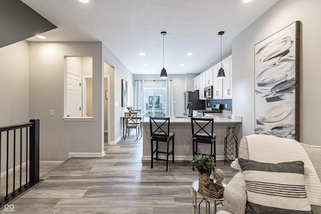 kitchen with light wood-style flooring, stainless steel appliances, white cabinets, light countertops, and a kitchen bar