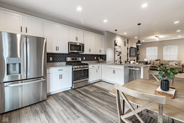 kitchen with open floor plan, stainless steel appliances, white cabinets, and light wood-style floors