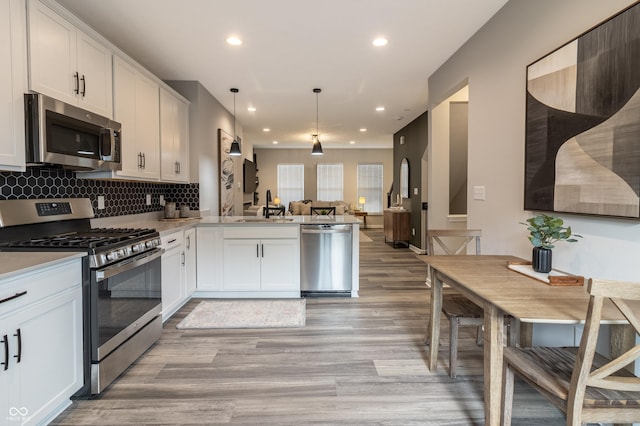 kitchen featuring light wood-style flooring, a peninsula, a sink, open floor plan, and appliances with stainless steel finishes