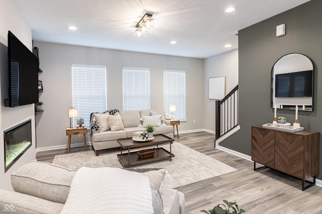 living room with recessed lighting, baseboards, stairway, light wood-type flooring, and a glass covered fireplace