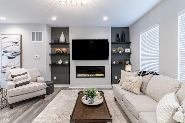 living area with recessed lighting, visible vents, wood finished floors, and a glass covered fireplace