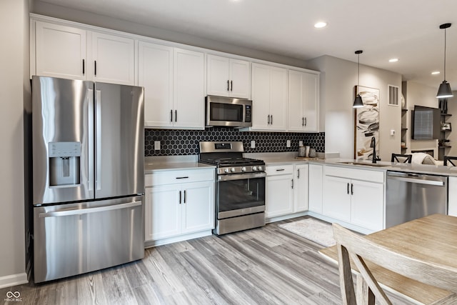 kitchen featuring tasteful backsplash, stainless steel appliances, light wood-style floors, white cabinetry, and a sink