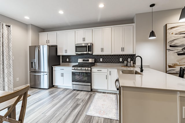 kitchen with a peninsula, a sink, appliances with stainless steel finishes, light wood finished floors, and tasteful backsplash