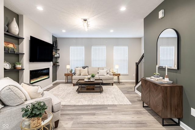 living area featuring baseboards, a glass covered fireplace, light wood-style flooring, and recessed lighting