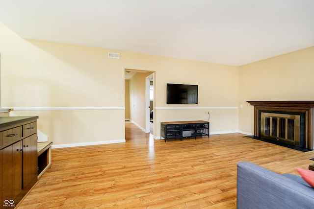 living room with light wood-type flooring, a wainscoted wall, a glass covered fireplace, and visible vents