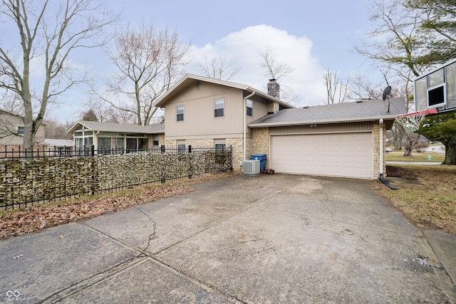 exterior space with concrete driveway, a chimney, an attached garage, fence, and cooling unit