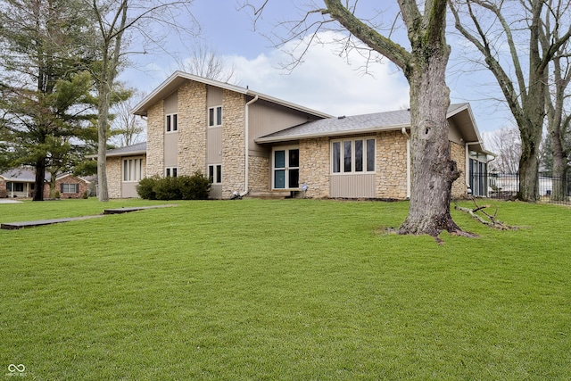 rear view of house featuring stone siding, a lawn, and fence