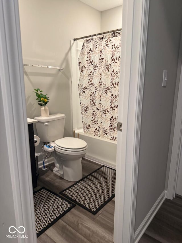 bathroom with baseboards, toilet, wood finished floors, and shower / tub combo