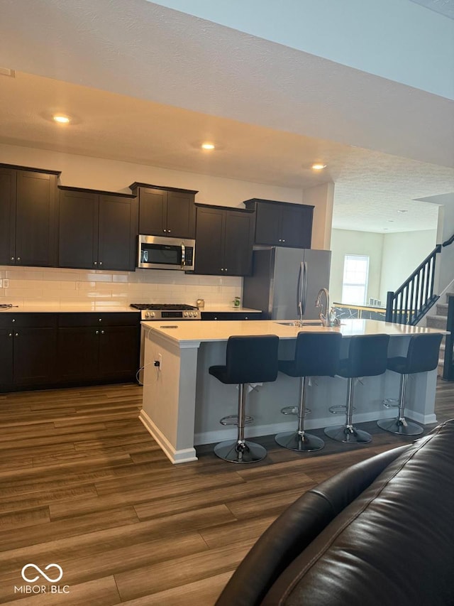 kitchen with decorative backsplash, a kitchen breakfast bar, dark wood-style flooring, and stainless steel appliances