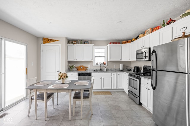 kitchen with appliances with stainless steel finishes, a sink, light stone countertops, and white cabinets