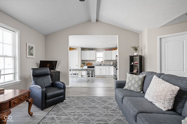 living area with baseboards, vaulted ceiling with beams, and light wood finished floors