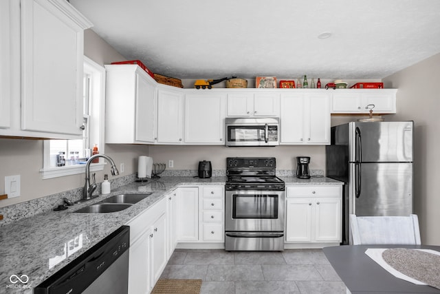 kitchen with light tile patterned floors, a sink, white cabinetry, appliances with stainless steel finishes, and light stone countertops