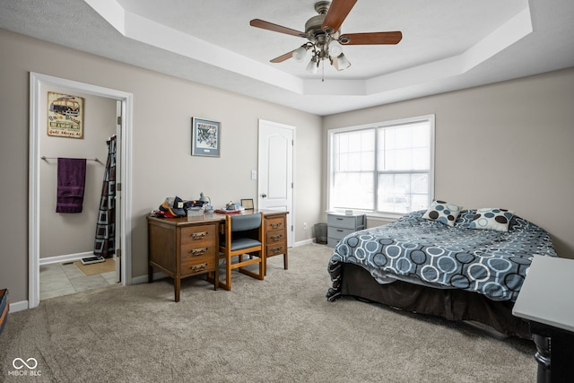 carpeted bedroom with a tray ceiling, ceiling fan, and baseboards