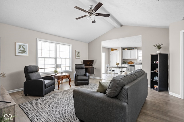 living area with baseboards, a healthy amount of sunlight, light wood-style flooring, and lofted ceiling with beams