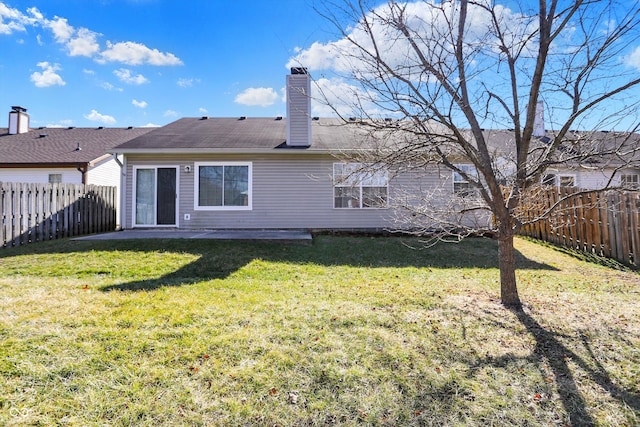 back of house with a fenced backyard, a lawn, and a chimney