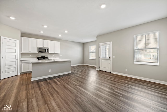 kitchen featuring baseboards, white cabinets, dark wood finished floors, open floor plan, and stainless steel appliances